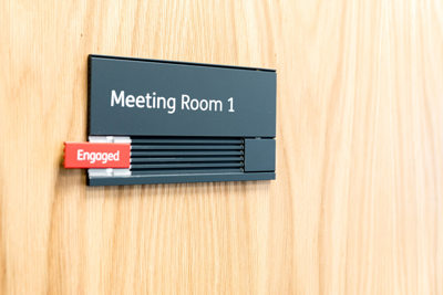 Image of a meeting room, with an 'engaged' sign on the door.