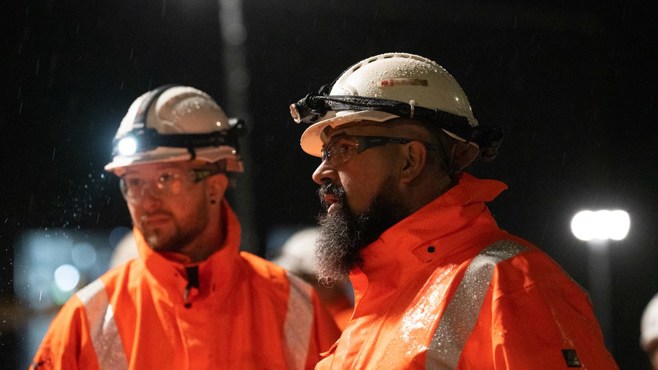 Two male Amey employees in the rain with PPE and headlamps 