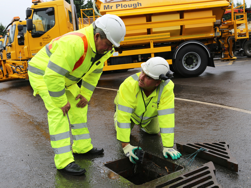 Two men in PPE, inspecting a drain.