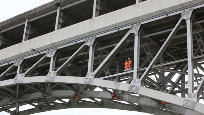 Men on ropes inspecting the underside of a bridge