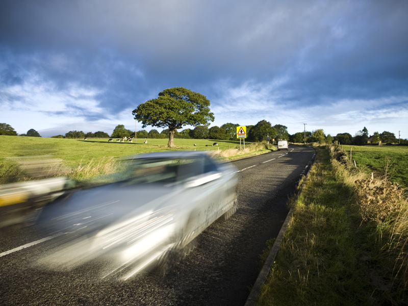 image of a car at speed on a rural road.
