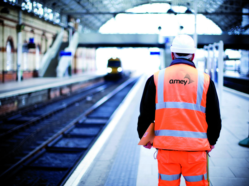 a man in PPE, stood at an empty train platform.