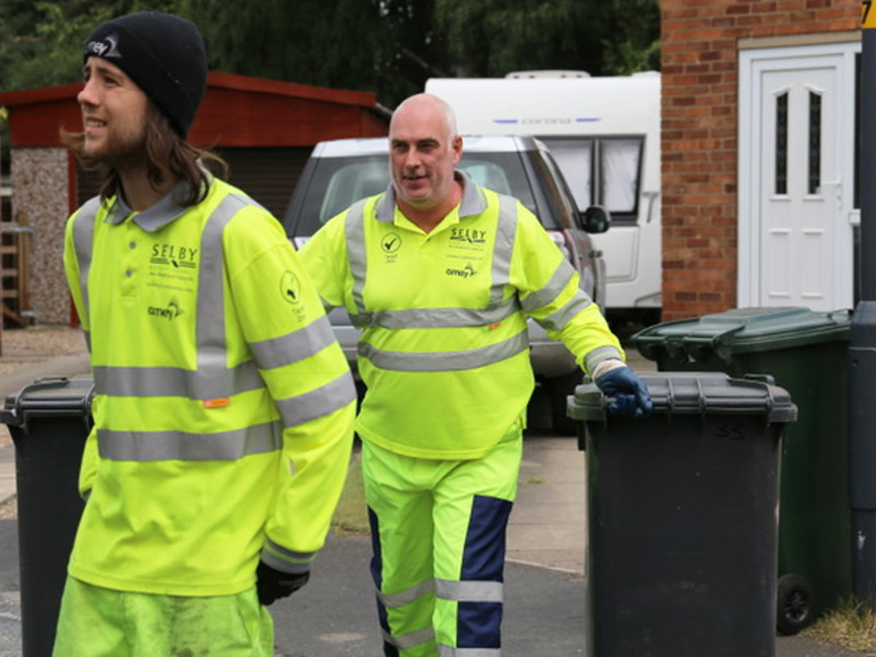 two men in PPE, moving bins.