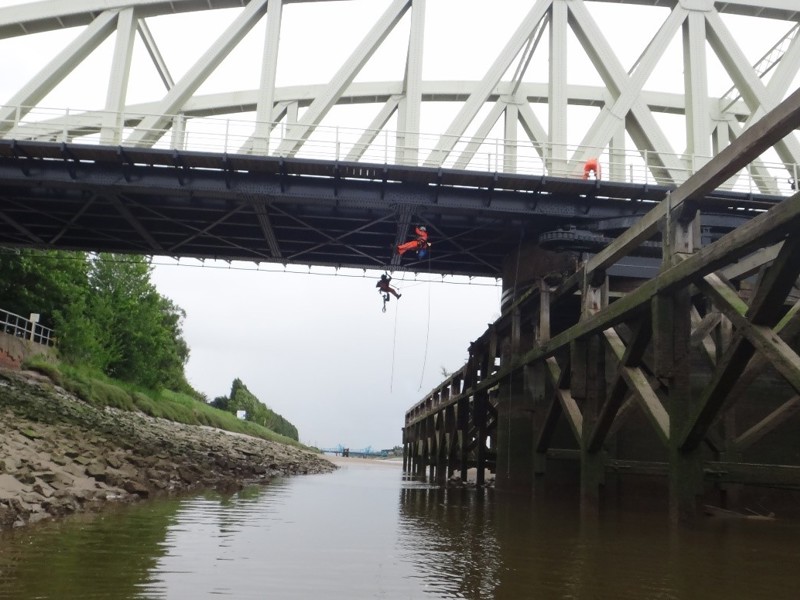 Men carrying out a bridge inspection, looking under the bridge hanging from safety equipment.