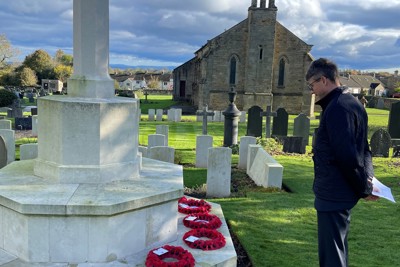 Image of a man standing at a poppy memorial in a cemetery.