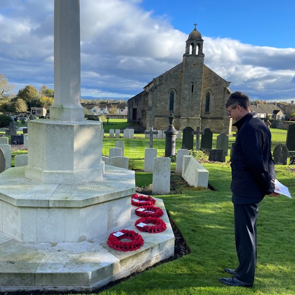 Image of a man standing at a poppy memorial in a cemetery.