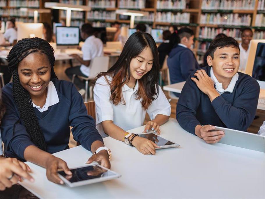 Three students in a classroom. Two are holding tablets.