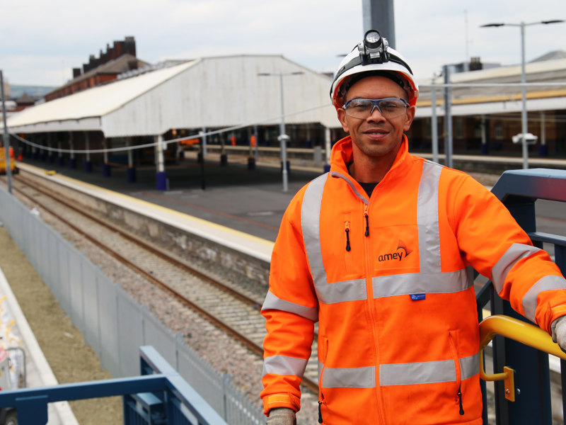 A man in PPE, stood at a railway.