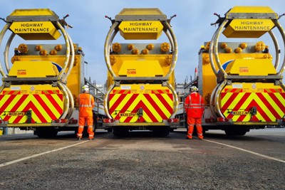 Three side by side highways maintenance vehicles, with a man in PPE stood between each one.