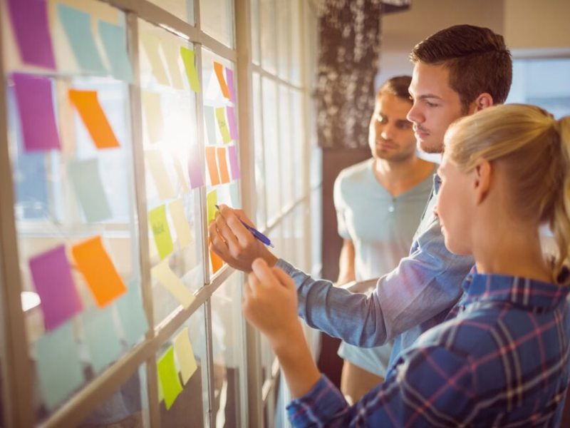 Image of a man and woman, writing on post-it notes placed on windows.
