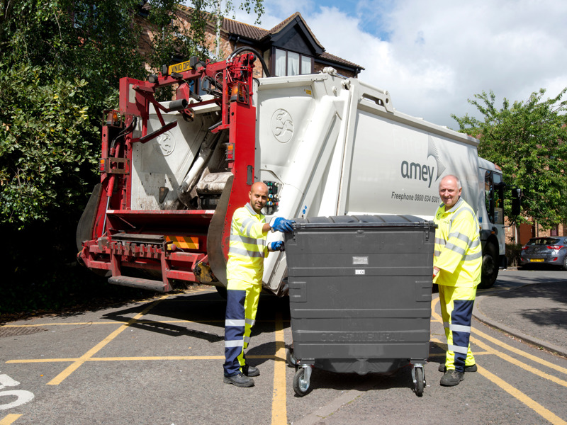 Image of two men moving an commercial waste bin.