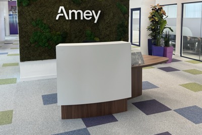A picture of the newly refurbished Amey reception desk at Liverpool’s Matchworks, featuring a moss-covered wall with the Amey logo, a modern curved desk, and colourful square-patterned carpet tiles.