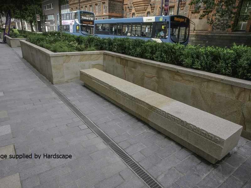 Image of a pathway with raised beds, and buses behind the wall.