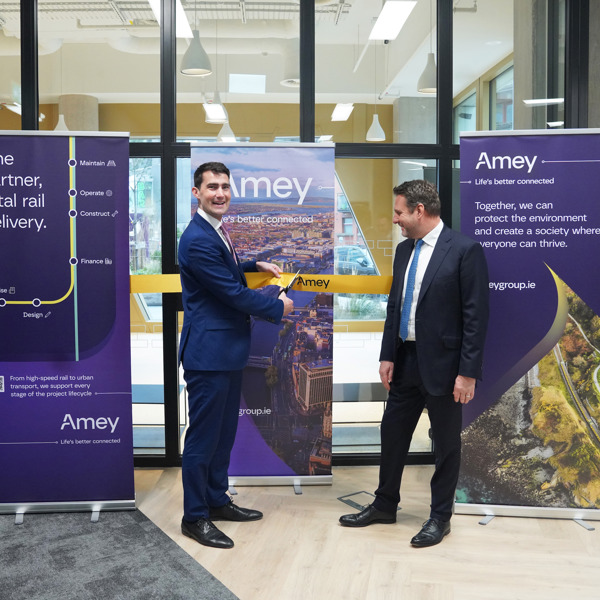 One man cuts an Amey branded ceremonial ribbon while a second man watches. Three Amey branded banners are placed behind them.