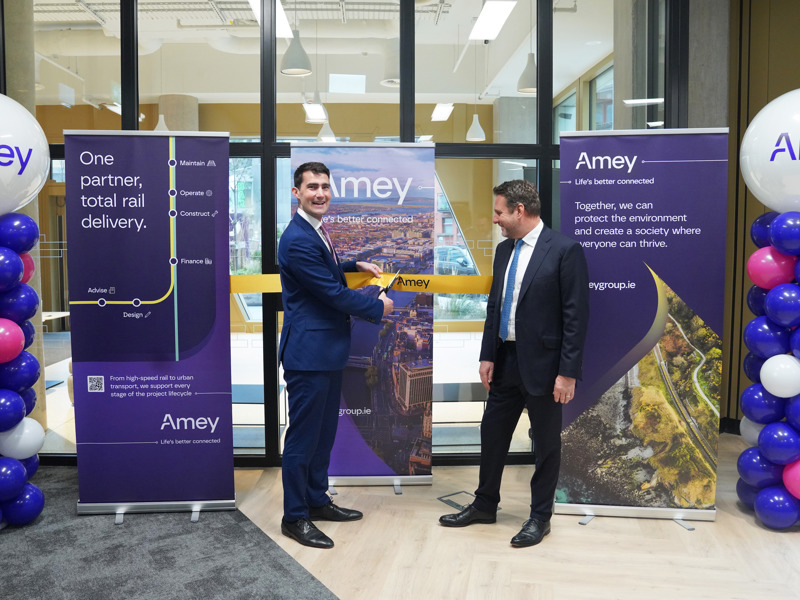 One man cuts an Amey branded ceremonial ribbon while a second man watches. Three Amey branded banners are placed behind them.