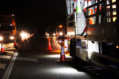 Night-time roadworks on a motorway with a maintenance truck, traffic cones, and Amey workers in high-visibility clothing.