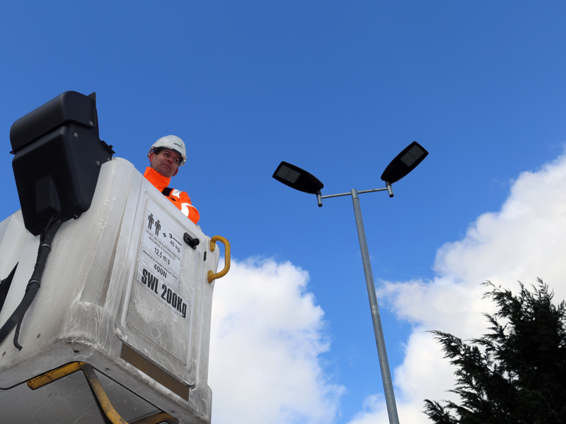 Man wearing PPE being lifted up in a crane to fix a streetlight.