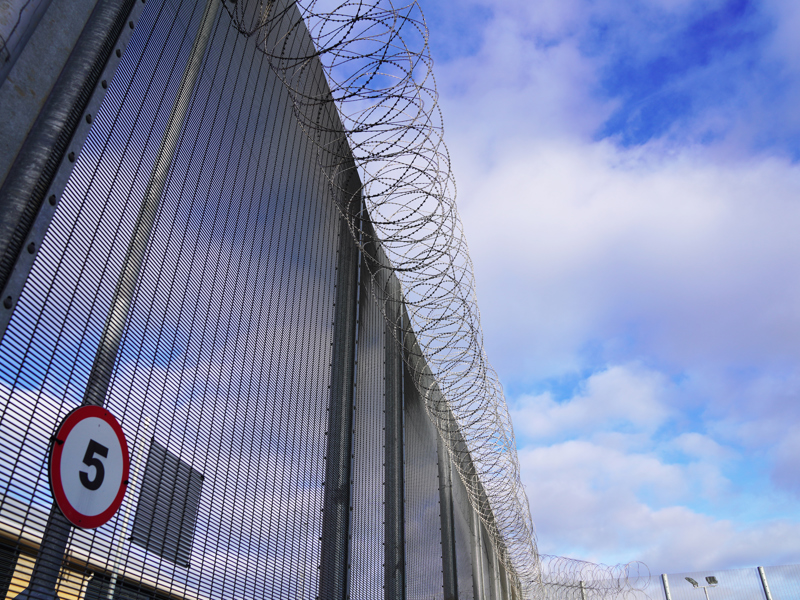 Image of a highly secured fence, topped with barred wire.